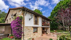 Una casa de piedra con balcón, jardín y cielo despejado.