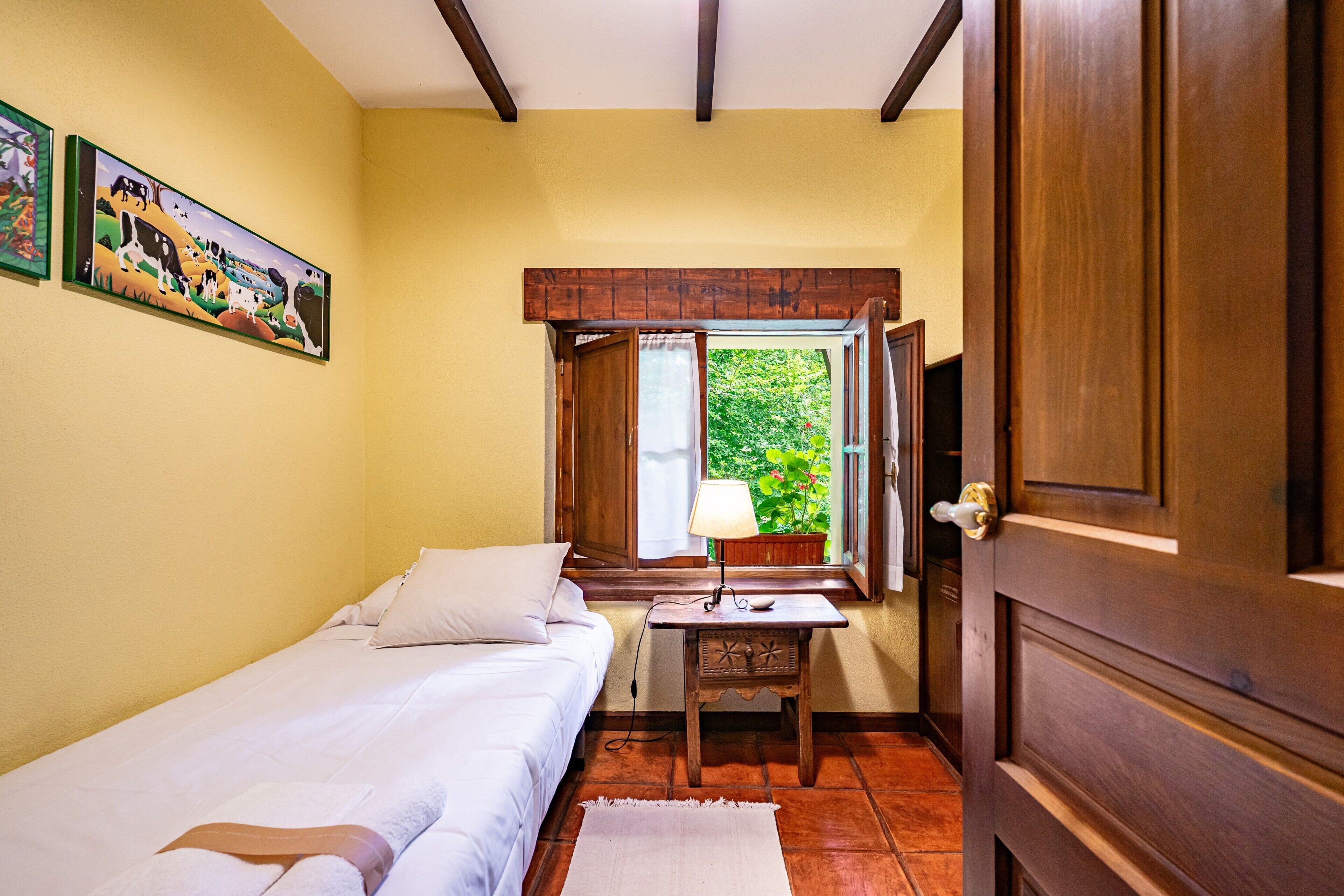 Una habitación con cama, una mesita de noche con lámpara, una ventana con cortinas y una puerta.