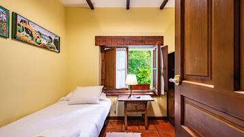 Una habitación con cama, una mesita de noche con lámpara, una ventana con cortinas y una puerta.