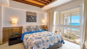 Un dormitorio con una cama grande, dos lámparas de noche, una mesita de noche, vistas al océano y un techo con vigas de madera.