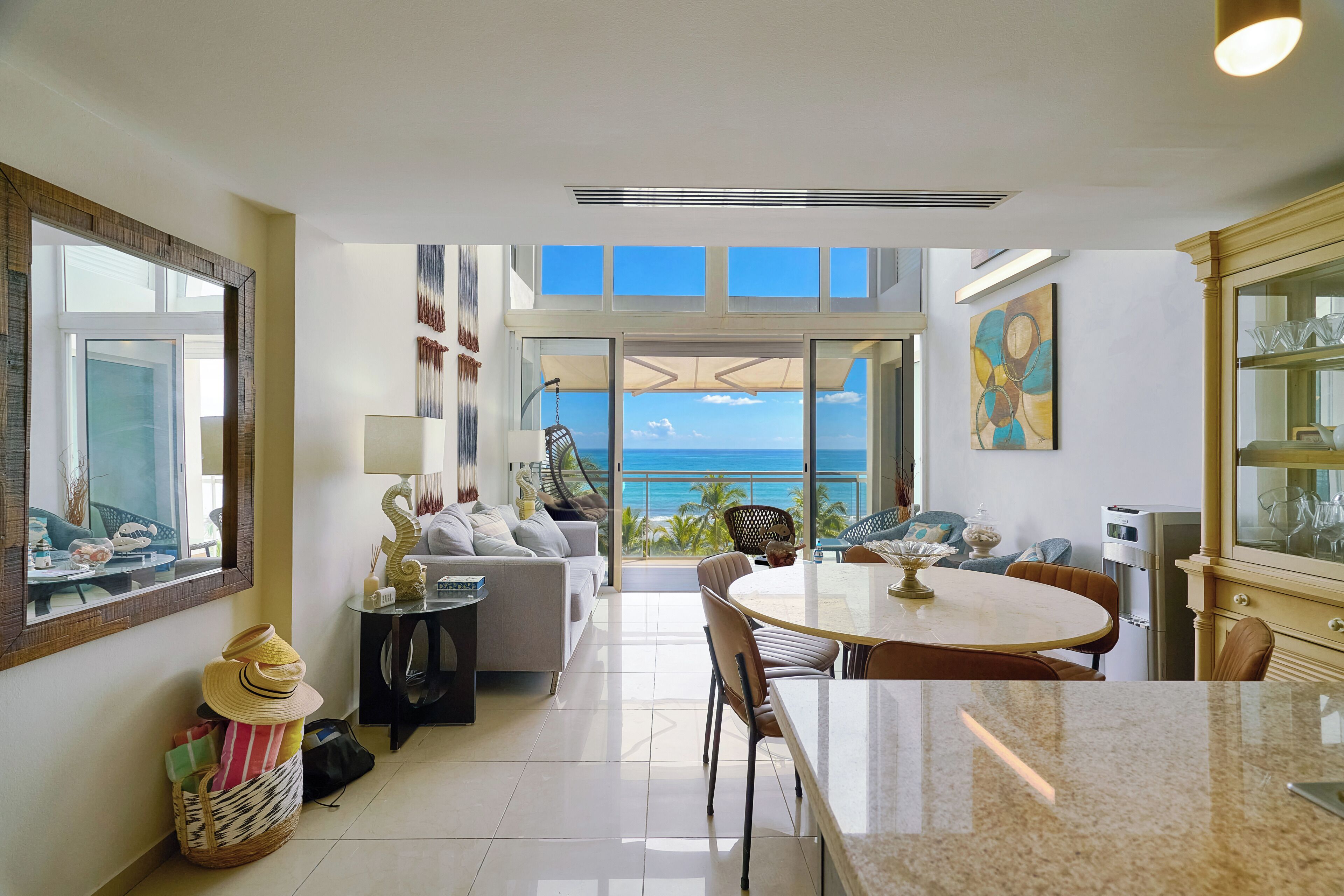 A modern interior with a dining area, kitchen, and large windows offering a view of the ocean.