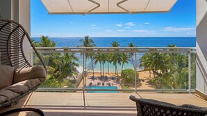 Un balcón con vista al océano, palmeras y una piscina.
