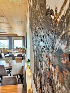 A restaurant with wooden ceiling, tables, chairs, and a large abstract painting on the wall. - Hotel Gasthof Kircher (Umes)