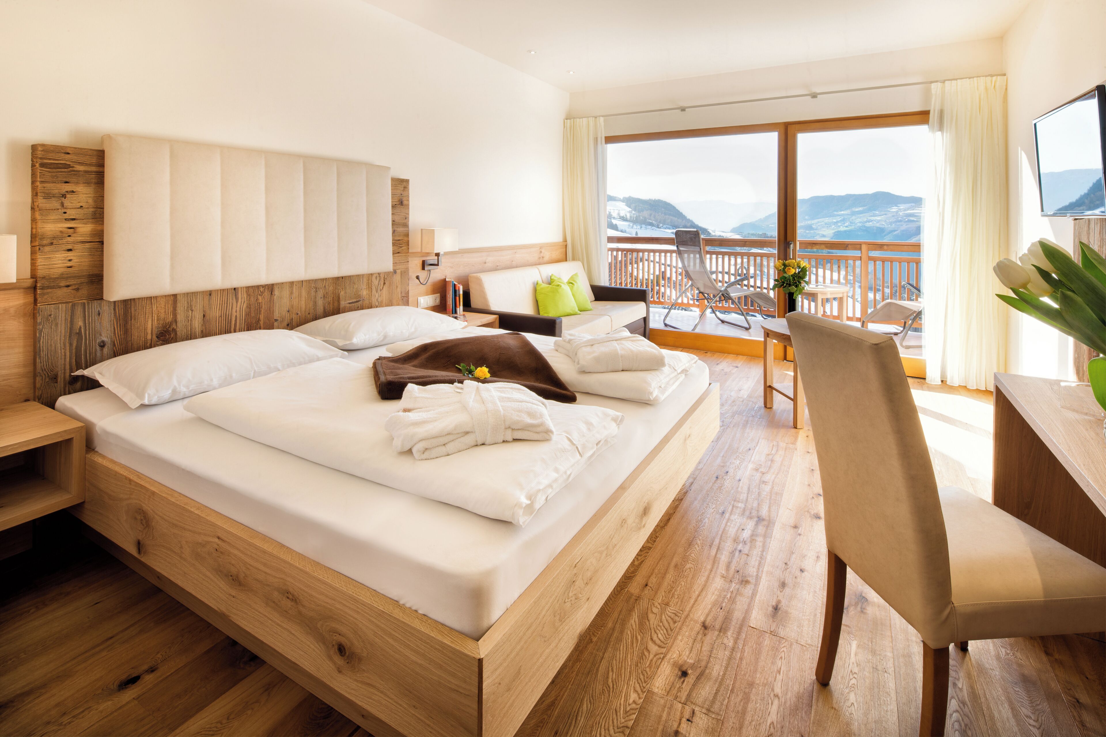 A hotel room with a wooden bed, a balcony with a view, a desk, and a chair.