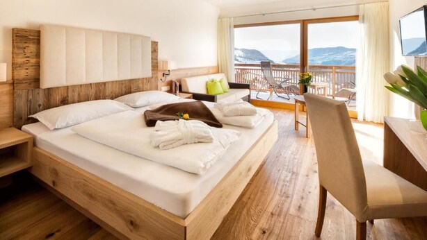 A hotel room with a wooden bed, a balcony with a view, a desk, and a chair. - Hotel Gasthof Kircher (Fie allo Sciliar)
