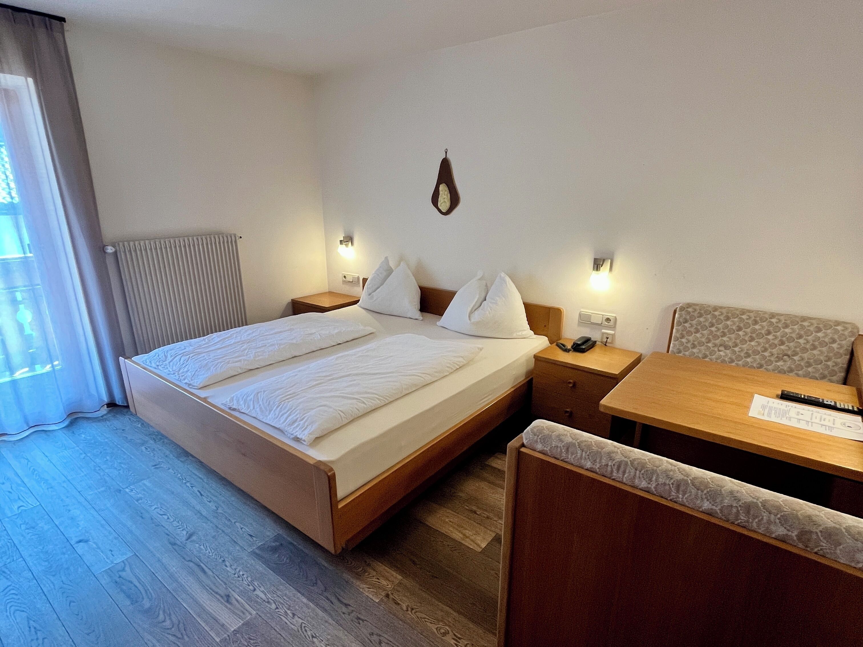 A hotel room with a bed, bedside table, chair, and a desk with a chair.