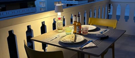 A dining table with chairs on a balcony with a city view at dusk.