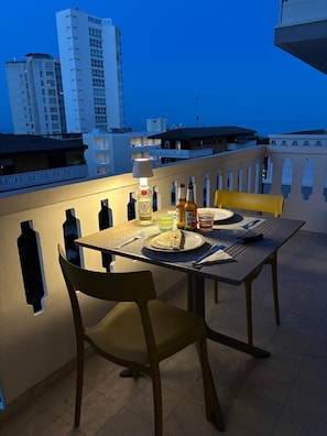 Ein Esstisch mit Stühlen auf einem Balkon mit Blick auf die Stadt im Abendlicht.