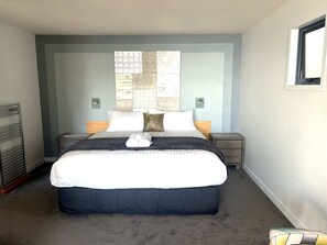 Ein Schlafzimmer mit einem großen Bett, zwei Nachttischen, einem Fenster und einer an der Wand befestigten Uhr.