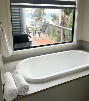 Ein Badezimmer mit Badewanne und einem Fenster mit Blick auf eine Terrasse und Gartenmöbel.