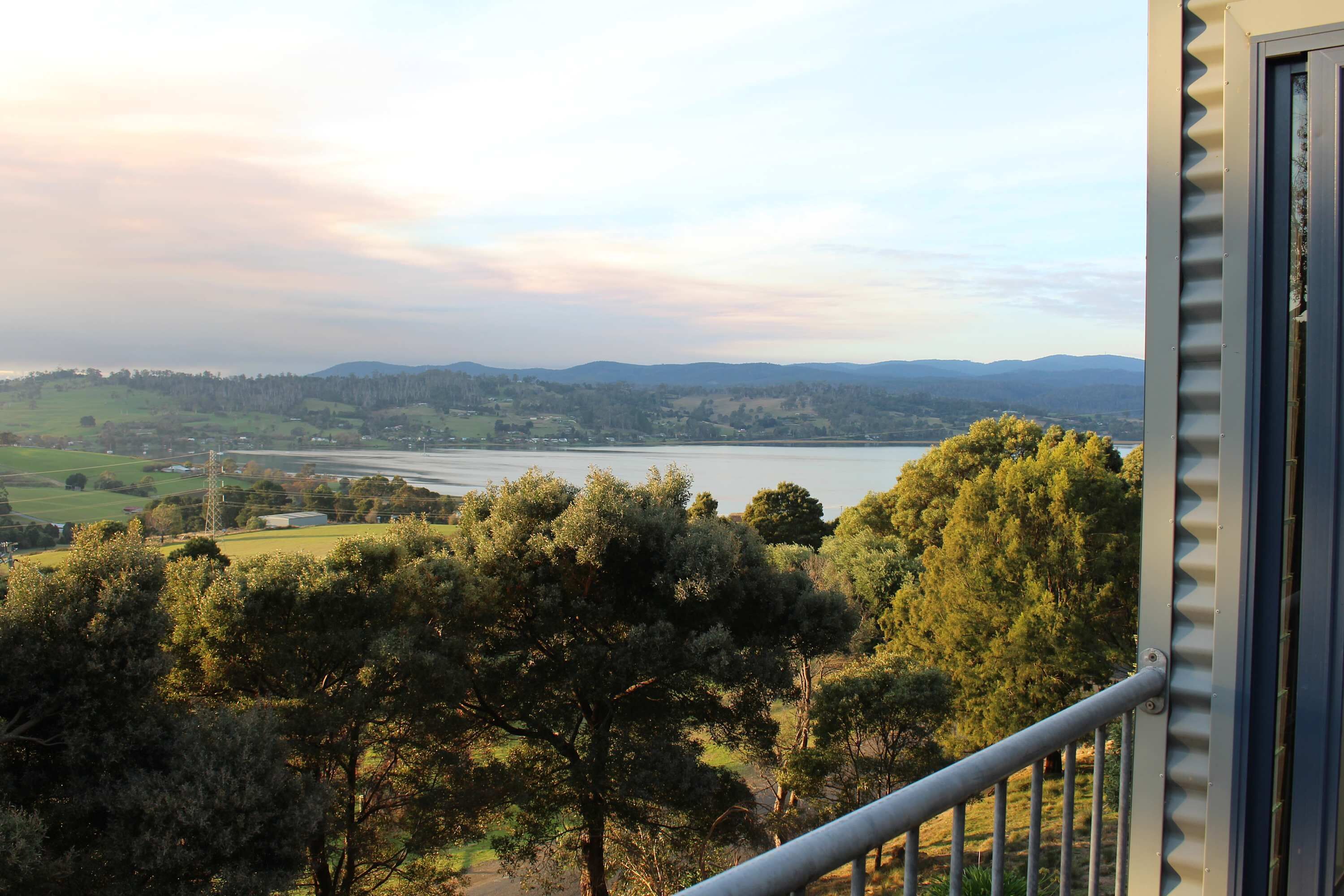 A view from a balcony overlooking a lake with trees and distant hills.