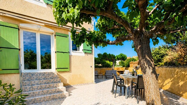 Ein Gebäude mit Pflasterterrasse, Außenbestuhlung und einem Baum.