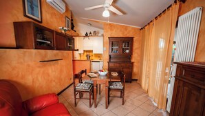 Une cuisine compacte avec un coin repas, comprenant un canapé rouge, des chaises en bois et un ventilateur de plafond.