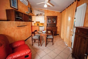 A compact kitchen with a dining area, including a red sofa, wooden chairs, and a ceiling fan.