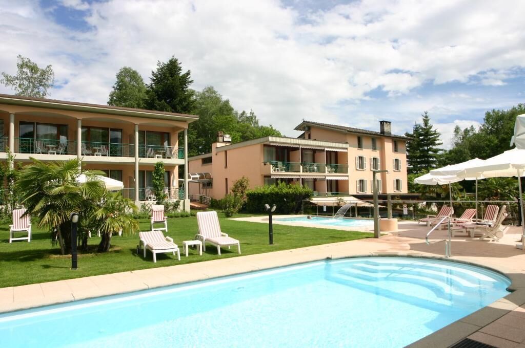 Ein Hotel mit Schwimmbad, Liegestühlen und einem gepflegten Rasen.