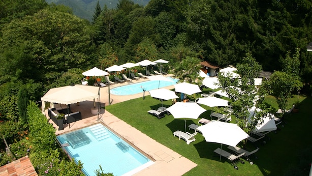 Ein Poolbereich mit mehreren Liegestühlen und Sonnenschirmen, umgeben von üppiger Vegetation und Bergen im Hintergrund.