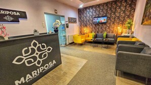 Un área de recepción con un letrero que dice Mariposa Boutique Apartments, un televisor montado en la pared y una zona de estar con sofás y mesas.