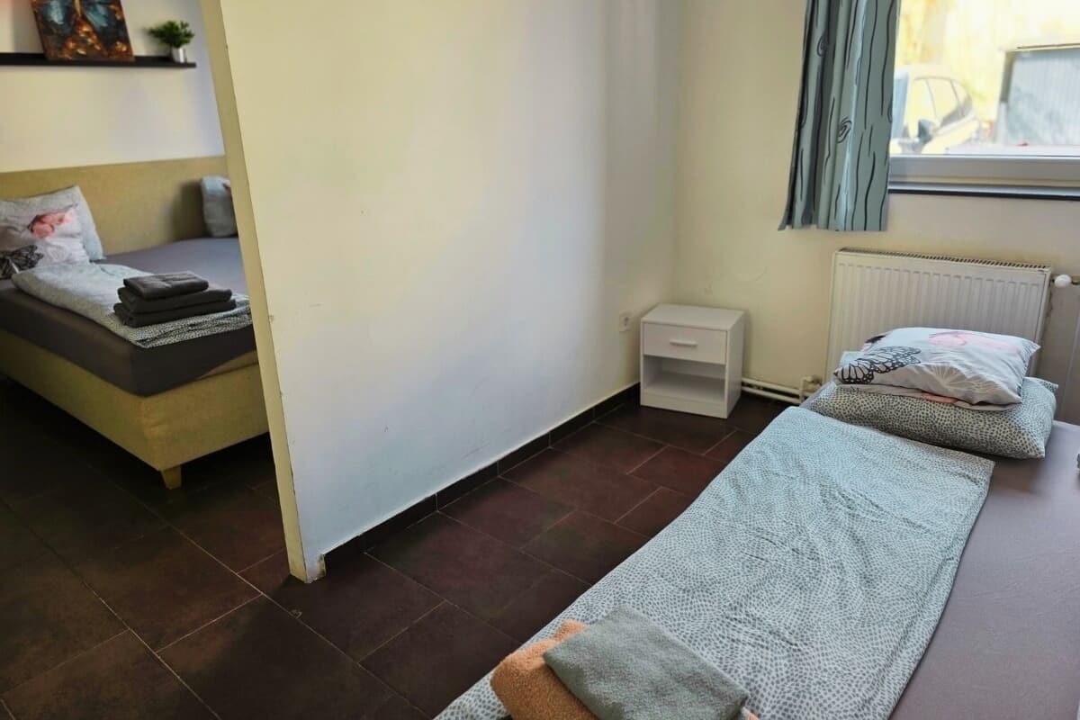 A single bed with a blanket, a bedside table, a radiator, and a window with curtains.