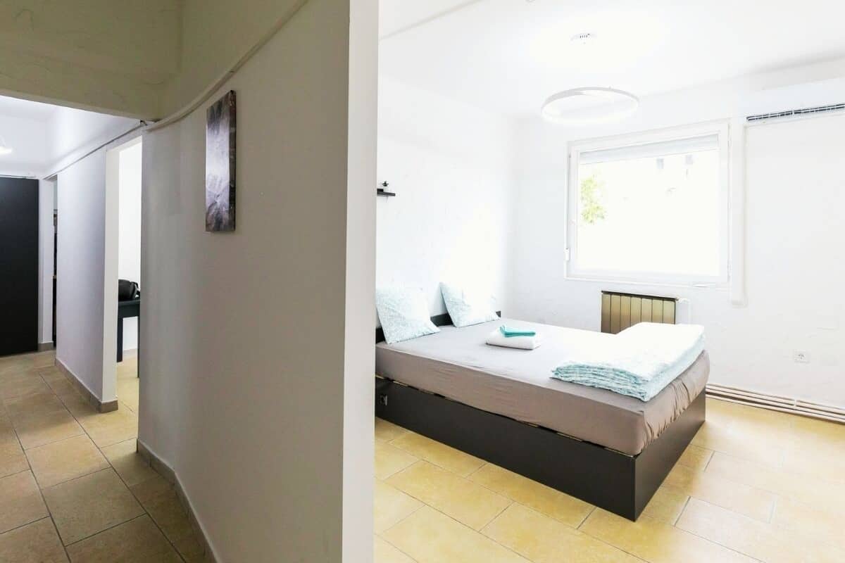A bedroom with a bed, a window, and a door leading to another room.