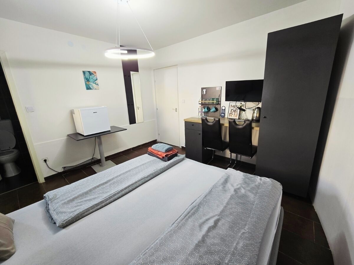 Quarto de hotel com uma cama, uma escrivaninha, uma cadeira, uma televisão e um guarda-roupa.