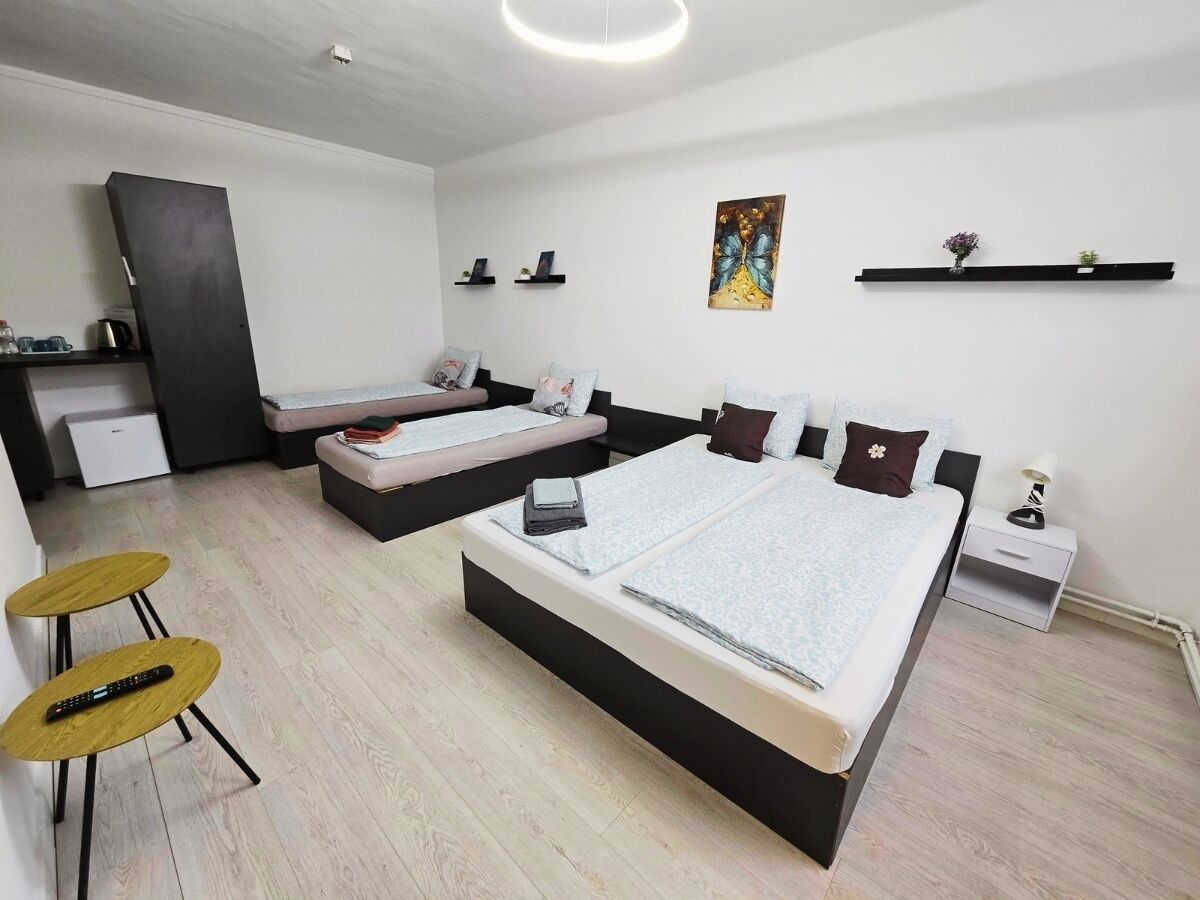 Una camera d'albergo moderna con due letti, un angolo cottura, un'area salotto con sgabelli e una mensola a parete con oggetti decorativi.