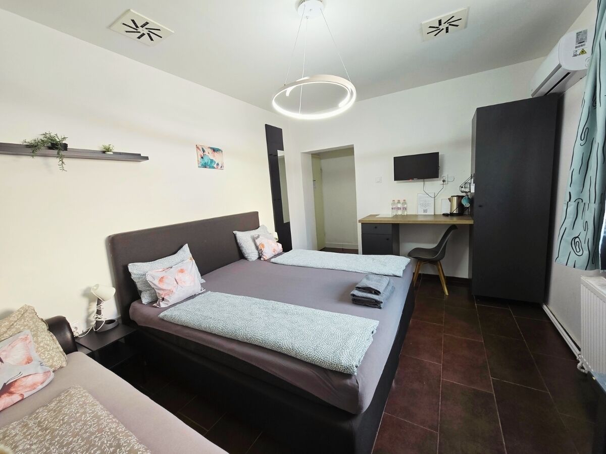 A bedroom with a bed, bedside tables, a desk, a chair, a TV, and a radiator.