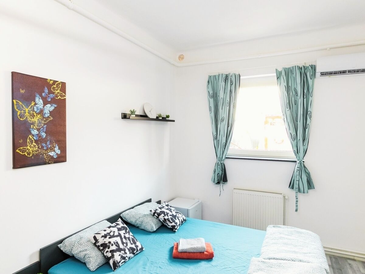 Un dormitorio con cama, almohadas, un radiador, una ventana con cortinas y una obra de arte en la pared.