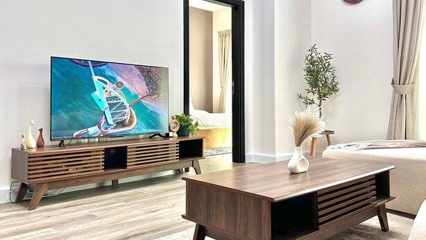 A modern living room with a flat-screen TV, wooden entertainment unit, and a sofa. - 2 Bedroom APT in Elite Sports Residence  (Dubai)