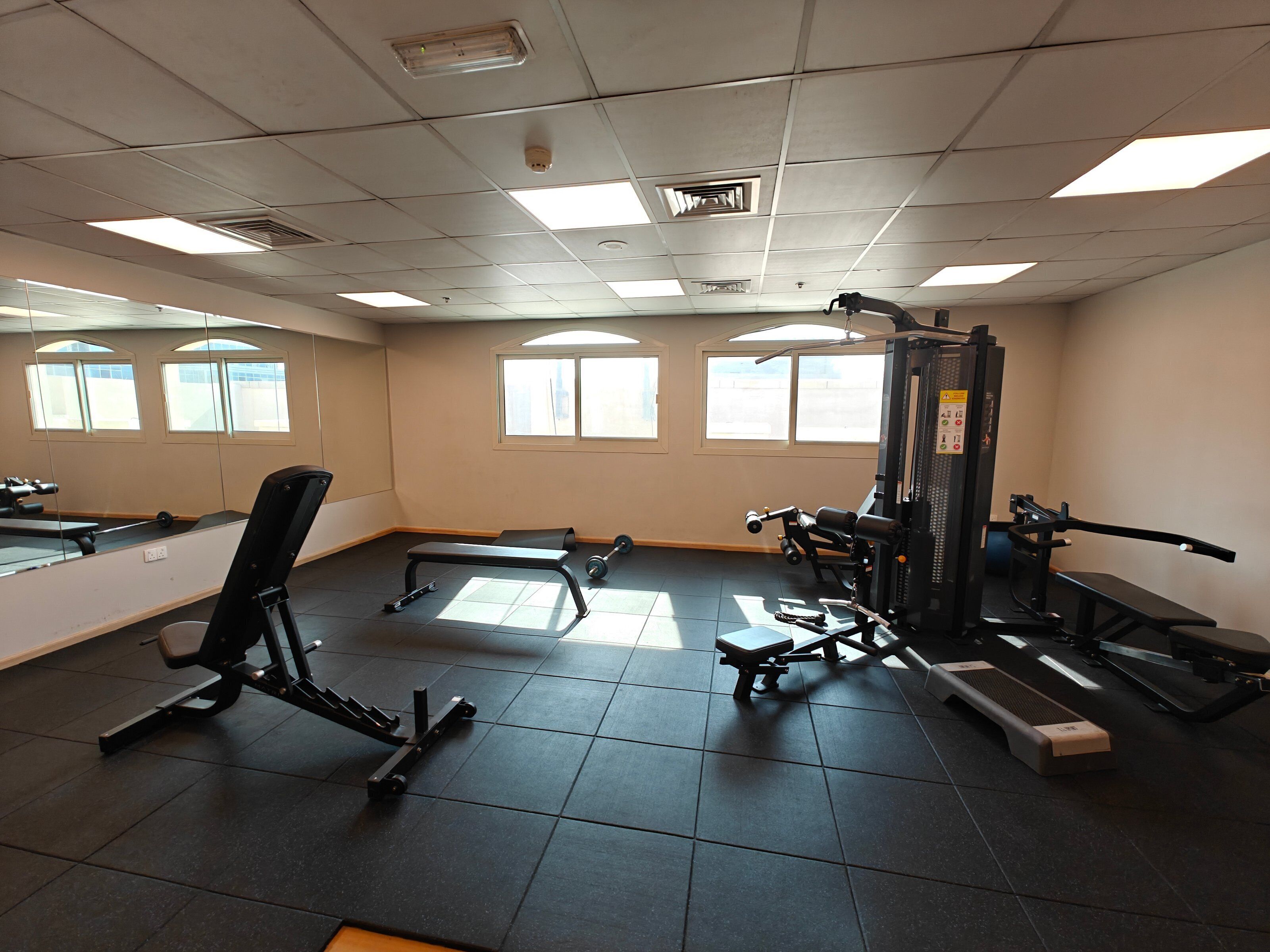 Un gimnasio con equipo de ejercicio, ventanas amplias y suelo de baldosas.