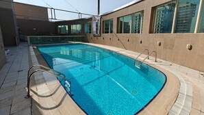 A swimming pool with clear blue water, surrounded by a tiled deck and a building with large windows. - 2 Bedroom APT in Elite Sports Residence  (Dubai)