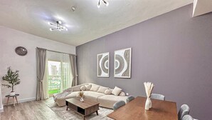 A modern living room with a sectional sofa, a wooden coffee table, a dining table with chairs, and two abstract wall art pieces. - 2 Bedroom APT in Elite Sports Residence  (Dubai)