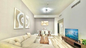 A modern living room with a sectional sofa, a dining table with chairs, a coffee table, a flat-screen TV, and artwork on the walls. - 2 Bedroom APT in Elite Sports Residence  (Dubai)