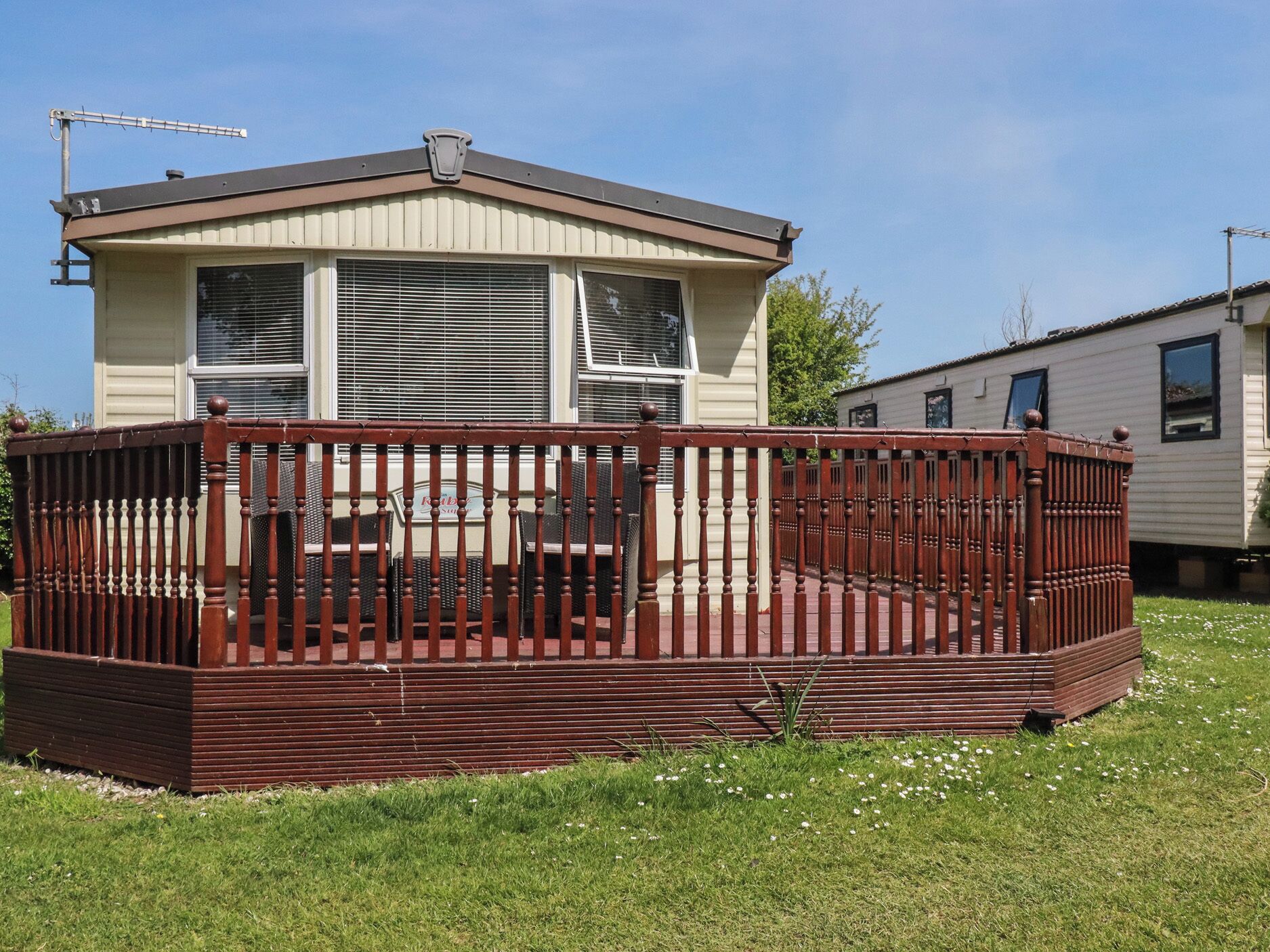 A mobile home with a fenced deck, a chimney, and a window with blinds.