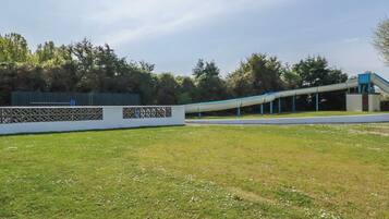 A grassy area with a white fence, trees, and a blue structure.