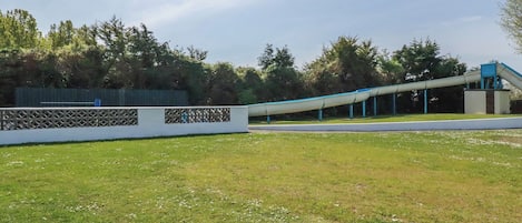 Un área cubierta de césped con una cerca blanca, árboles y una estructura azul.
