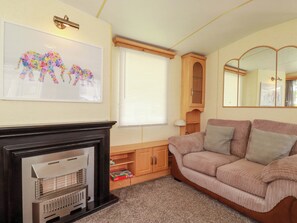A living room with a fireplace, a sofa, a cabinet, a mirror, and a framed picture on the wall. - Beech Lodge (Wadebridge)