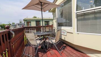 Eine überdachte Terrasse mit Tisch und Stühlen, ein Holzboden und ein Fenster mit Jalousien.
