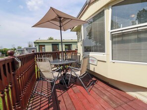 Eine überdachte Terrasse mit Tisch und Stühlen, ein Holzboden und ein Fenster mit Jalousien.