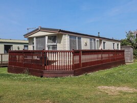 A mobile home with a fenced yard, a small shed, and a grassy area with white flowers.