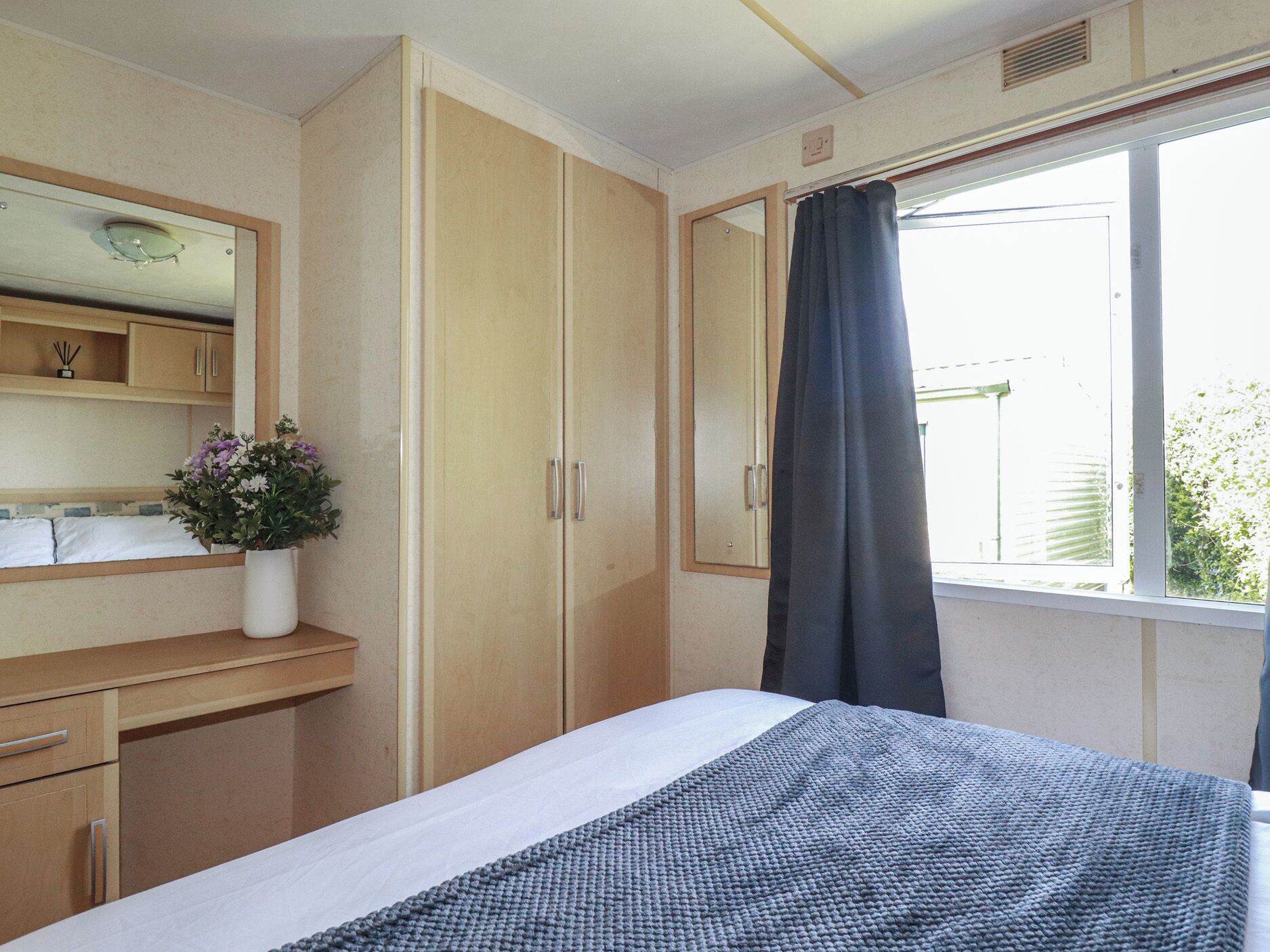 Un dormitorio con cama, cómoda, espejo, ventana con cortinas y una planta en maceta.