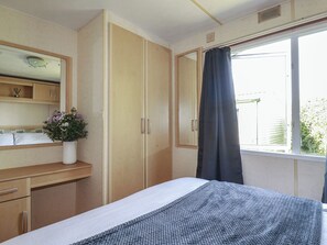 Ein Schlafzimmer mit einem Bett, einem Schminktisch, einem Spiegel, einem Fenster mit Vorhängen und einer Zimmerpflanze.