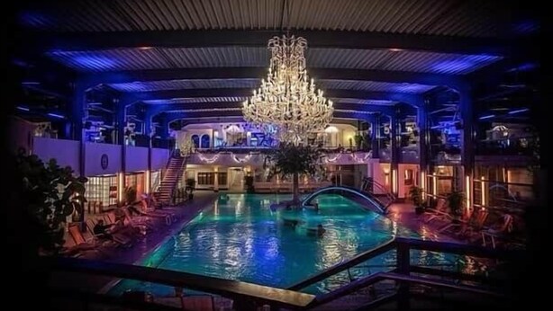 Une piscine intérieure agrémentée d’un lustre, entourée de chaises longues et d’un escalier.