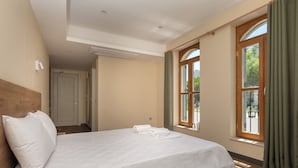 Une chambre à coucher avec une tête de lit en bois, un grand lit recouvert de draps blancs, une fenêtre avec des rideaux et une porte donnant sur une autre pièce.