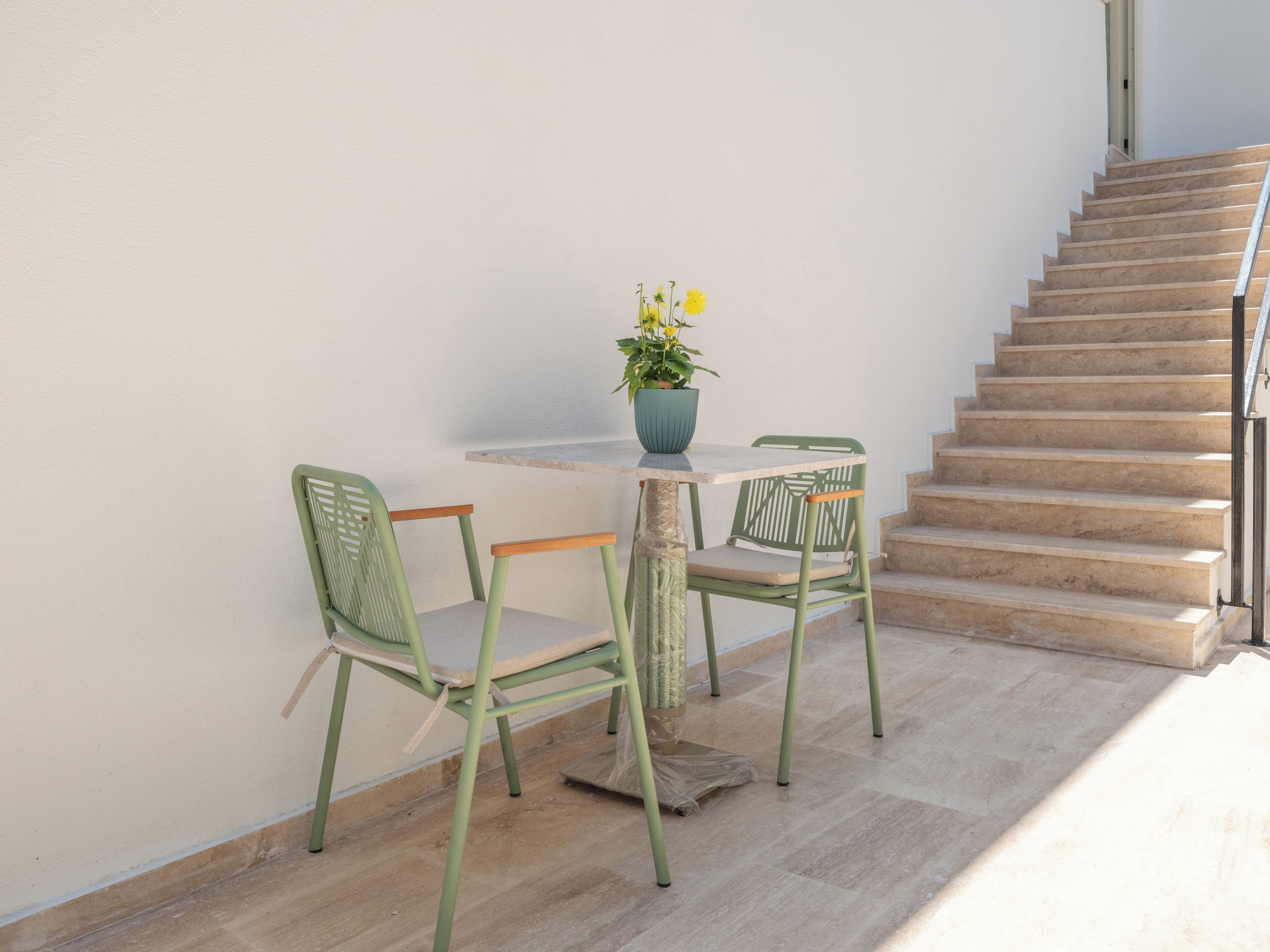 A staircase leading to an upper floor, a small outdoor table with chairs, and a potted plant with yellow flowers.