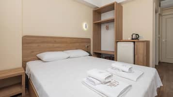 Habitación de hotel con cama de cabecera de madera, armario empotrado, kitchenette pequeña y mesita de noche.