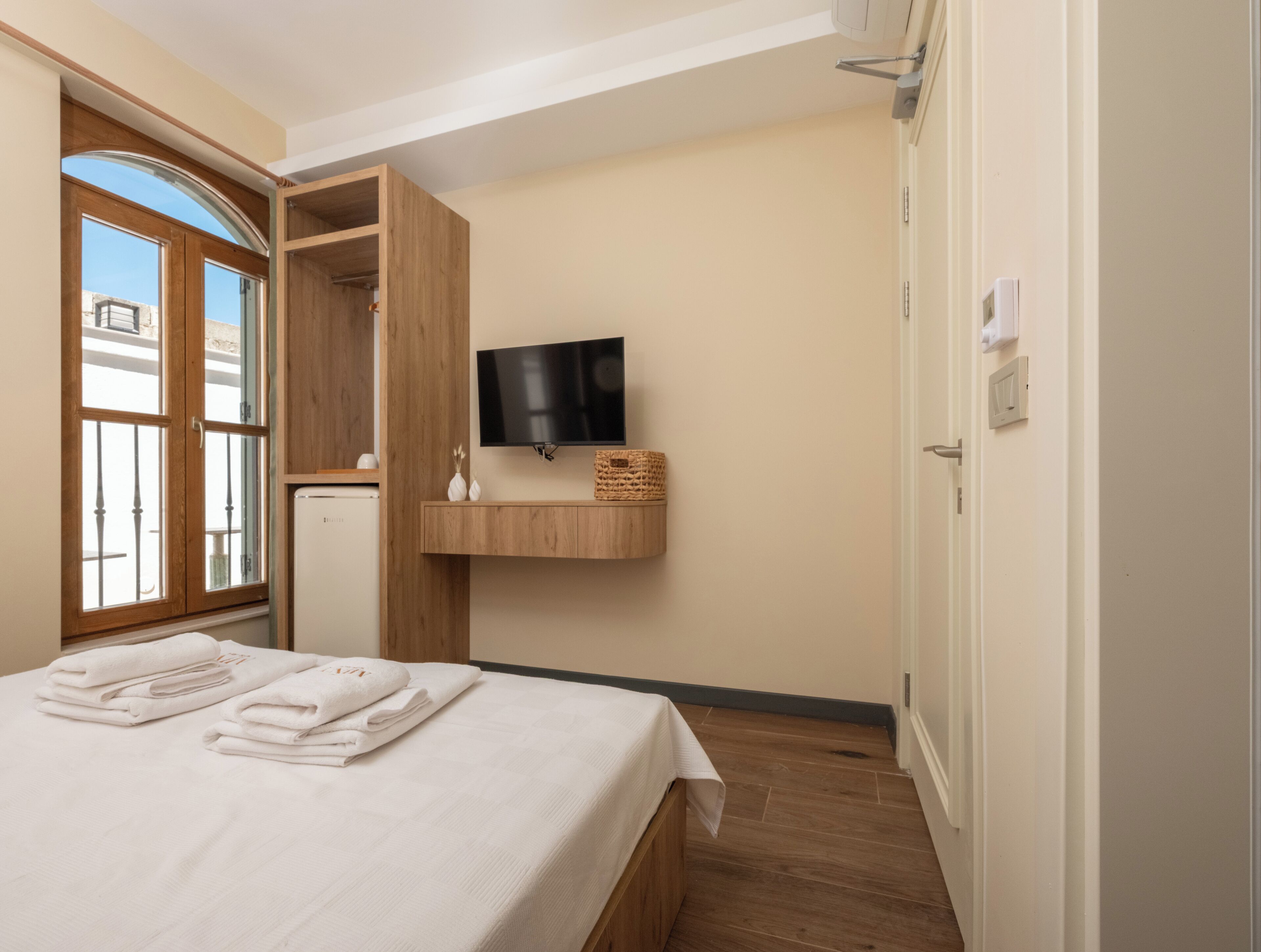 Un dormitorio con cama, televisor, armario de madera y ventana.
