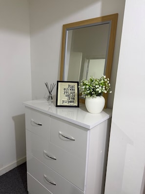 A white dresser with a mirror, a framed inspirational quote, and a vase with white flowers.