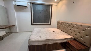 A bedroom with a bed, a window, a ceiling fan, and a bedside table. - Jeet residency by twamev (New Delhi)