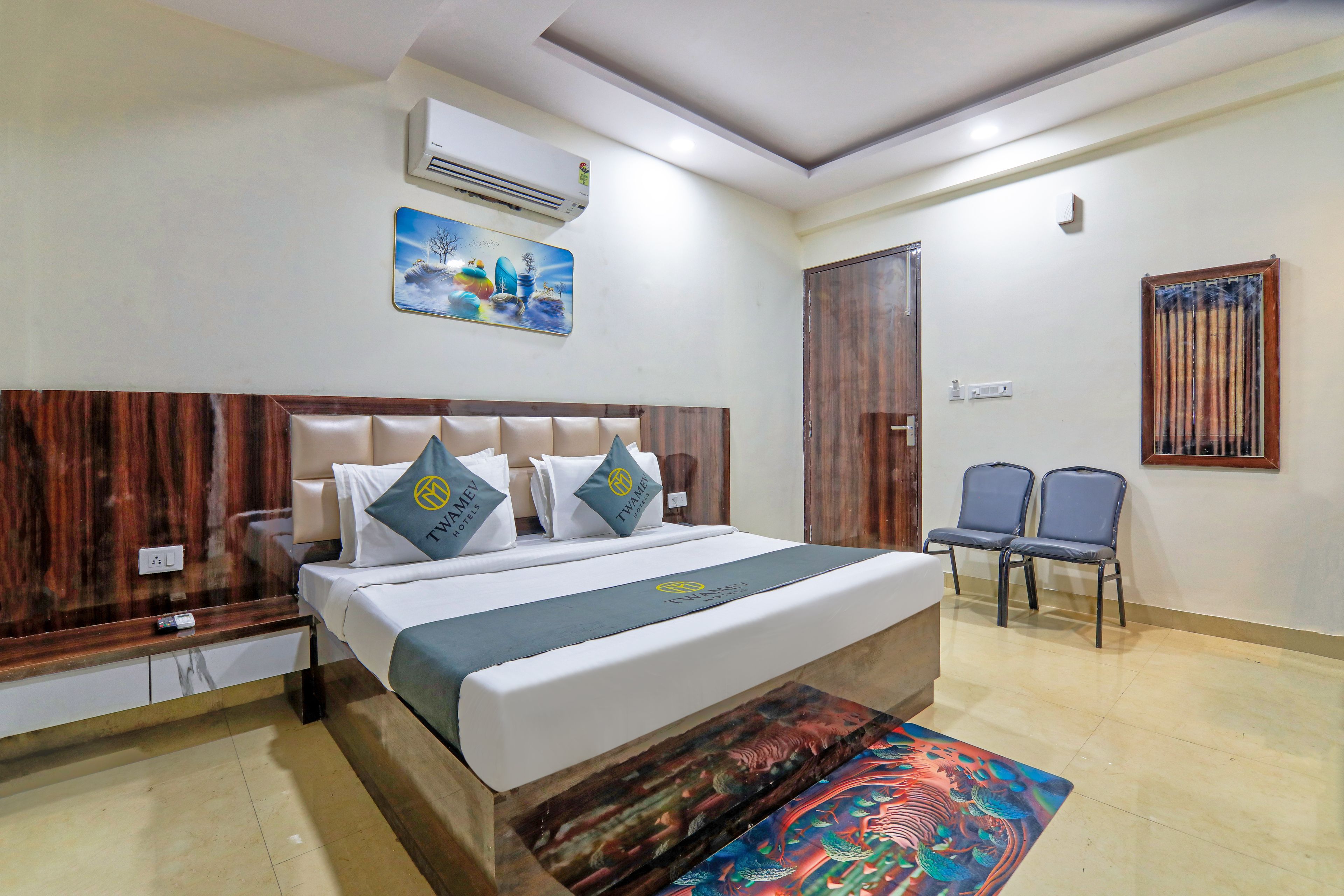 Quarto de hotel com cama, duas cadeiras, ar condicionado, um quadro e uma porta.