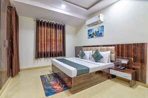 A hotel room with a bed, bedside table, and an air conditioning unit. - Jeet residency by twamev (New Delhi)
